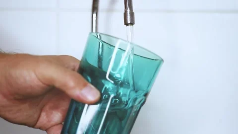 A jet of water flows into a glass. Drinking water from a tap. The man is fetc Stock Footage 218006833