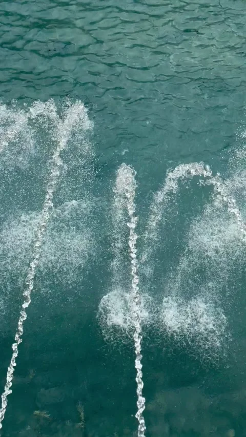 Jets of water rise and fall against calm green-blue water Stock Footage 334705329