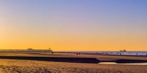 Jetty with lighthouse and a ship in the sea at sunset, the beach of blankenbe Stock Photos