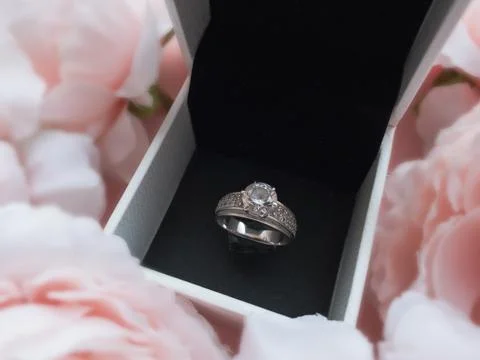 In the jewelry box there is a ring in a frame of pink delicate peonies on a b Stock Photos