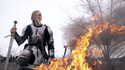 Joan of Arc in armor sits by the fire and looks around, slow motion Stock Footage