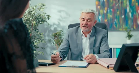 Job interview elderly boss with gray hair sitting at desk opposite him woman Vídeo Stock 164895170