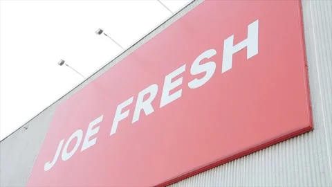 Joe fresh sign logo rectangle orange white mounted on wall with lights above Stock Footage 252042423