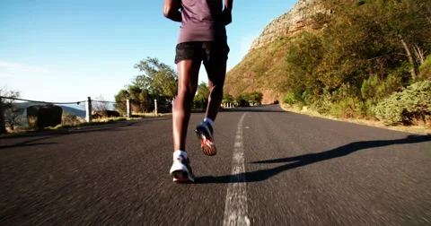 Jogger running along mountain road in slow motion Stock Footage