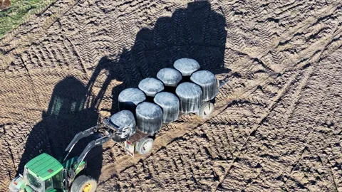 John Deere farm tractor stacking silage bales on trailer in field, aerial view Stock Footage 337790913