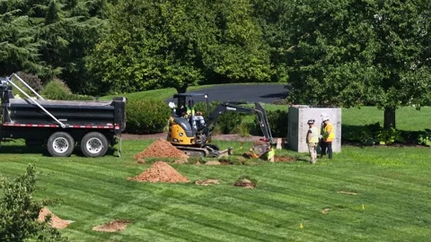 John Deere mini excavator digs trench beside black dump truck during natural Stock-Footage 344564608