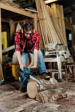 Joiner in the workshop saws the tree with an electric chainsaw. carpenter in the Stock Photos
