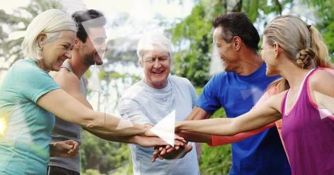 Joining six adults stacking hands in park, wearing athletic tops, play-button Stock Photos
