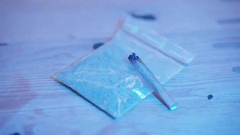 Joint and baggie of illegal marijuana on a table with flashing red and blue Vidéo 335151670