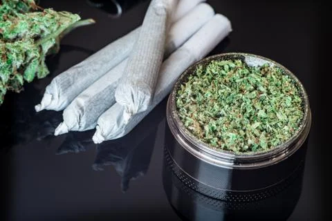 Joint and a grinder with crushed weed cannabis, buds of marijuana, on a black Stock Photos