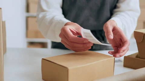 Joint venture, Warehouse worker Focusedly sticking a barcode on a cardboard Stock Footage 233815840