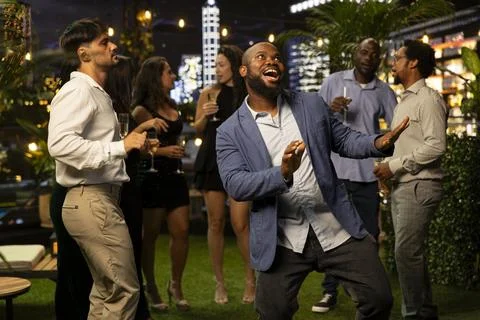 Jolly man doing funny dance moves on rooftop terrace, entertaining his friends Stock Photos
