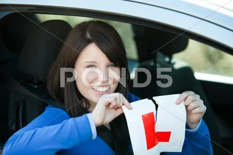 Jolly teen girl sitting in her car tearing a L-sign Stock Photos