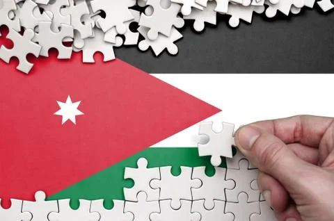 Jordan flag  is depicted on a table on which the human hand folds a puzzle of Foto stock