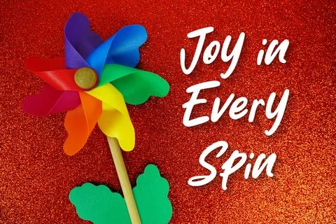 Joy in Every Spin text with colorful windmill on red glitter background Stock Photos