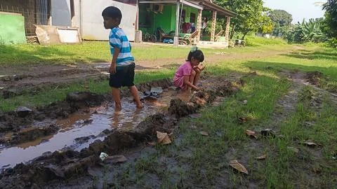 The joy of three small children playing with water and mud on a dirt road. Stock Photos