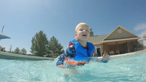 Joyful 4 year old boy in pool throws his body toward camera, splashing water Stock Footage 248080919