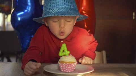 Joyful 4-year-old boy blows out candle shaped like number four on a small Stock Footage 316084583