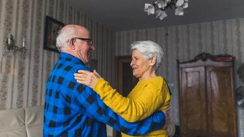 Joyful active old couple dancing and laughing in the living room, having fun at Stock Photos