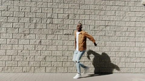 Joyful Afro-American guy walking in street then jumping and laughing outdoors Stock Footage 161386429
