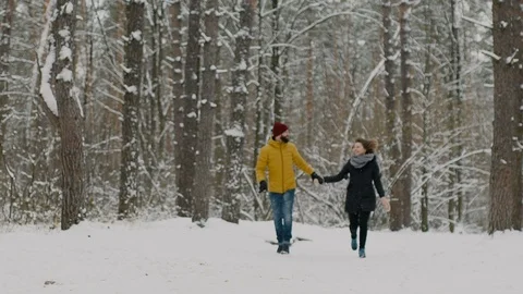 Joyful and happy, warmly dressed guy and girl holding hands running through the Vidéo 99779862