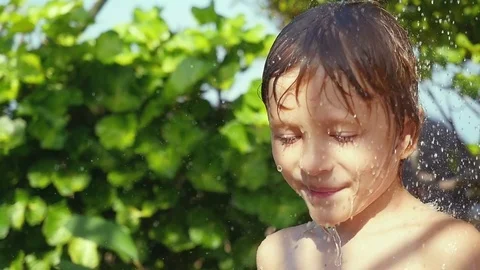 Joyful boy playing with water in the garden, boy has a shower and washing his Stock Footage