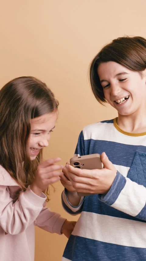 Joyful brother and sister using smartphone together. Vertical Stock Footage 341269704