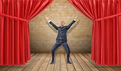 A joyful businessman standing at a wooden stage between red curtains in a Stock Photos