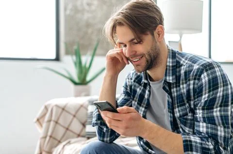 Joyful caucasian attractive guy using his smartphone while sitting on sofa at Fotos de archivo