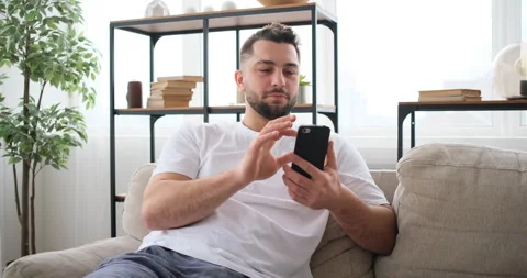 Joyful caucasian man using smartphone on sofa in living room Stock Footage 150019313