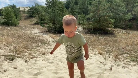 A Joyful Child Engaged in Play on Sandy Terrain Surrounded by Lush Green Trees Stock Footage 308333482