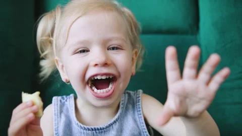 Joyful child enjoying snack while sitting on a green chair in a cozy indoor Stock Footage 308490113
