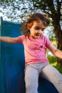 Joyful child glides down the slide in a sunlit park Stock Photos