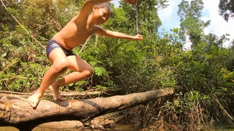 Joyful child jumping to the river from fallen tree trunk and water splashes arou Stock Footage 125920307