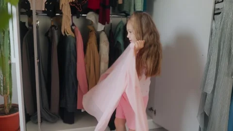 Joyful child wraps herself in a large oversized adult pink blouse at home. 库存影片 336668081