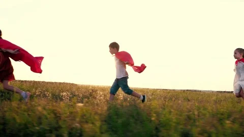 Joyful children group with red hero capes runs across rural field at back sunset Stock Footage 252000945