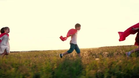 Joyful children group with red hero capes runs across rural field at back sunset Stock Footage 252233589