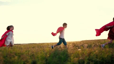 Joyful children group with red hero capes runs across rural field at back sunset Stock Footage 252545352