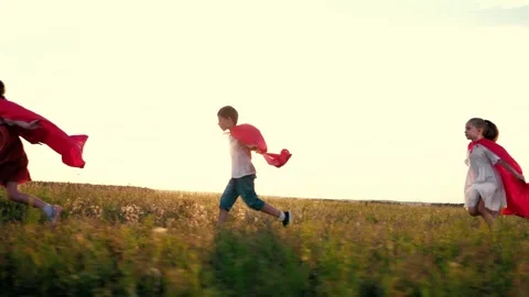 Joyful children group with red hero capes runs across rural field at back sunset Stock Footage 252545362