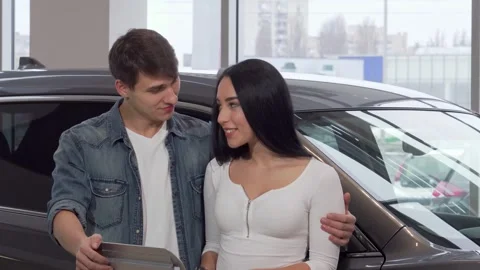 Joyful couple embracing while proudly holding car keys at a vibrant dealership Video stock 311647537