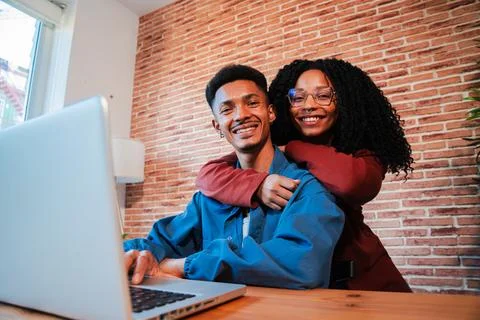 Joyful Couple Embracing While Working Together on a Laptop in a Cozy Home Stock Photos
