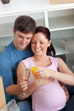 Joyful couple expecting a baby drinking and sitting on the floor Stock Photos