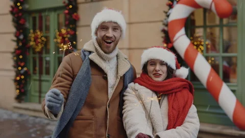 Joyful couple holding sparklers while standing on decorated xmas street in good Stock Footage 221443510