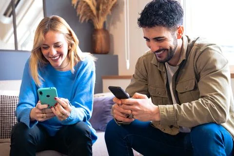 Joyful couple laughing while using smartphones at home, casual moment Stock Photos