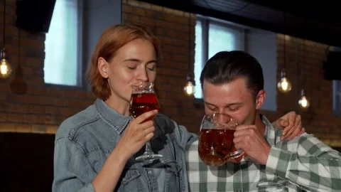 Joyful couple sharing laughter and clinking glasses of beer at a cozy pub Stock Footage 311658587