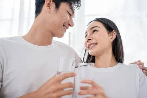 Joyful couple sharing a moment while holding glasses of water in a bright a.. Stock Photos