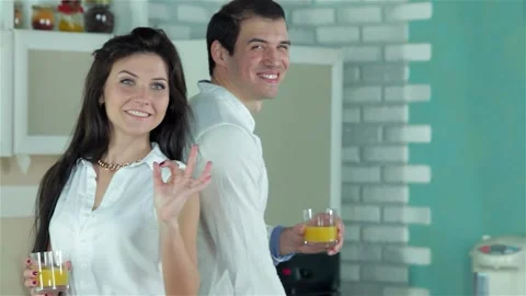 Joyful couple standing back to back, holding refreshing orange juice, the girl Stock Footage 311813300