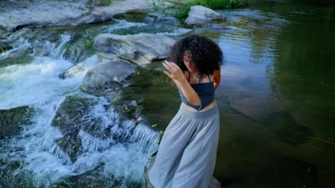 A joyful dancer gracefully performs by the soothing waters of a serene stream Stock Footage 314876910