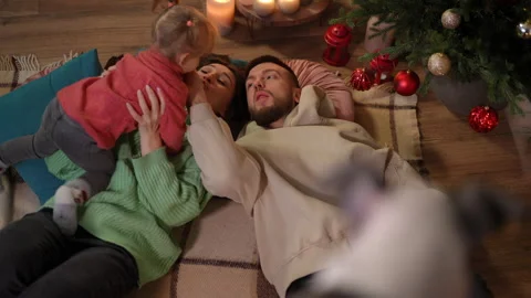 Joyful daughter having fun with young mother and father lying at Christmas tree Stock Footage 219909771