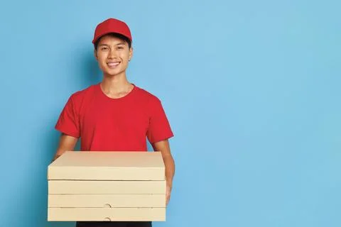 Joyful delivery guy dressed in red cap and red t-shirt holding boxes with pizza Foto stock